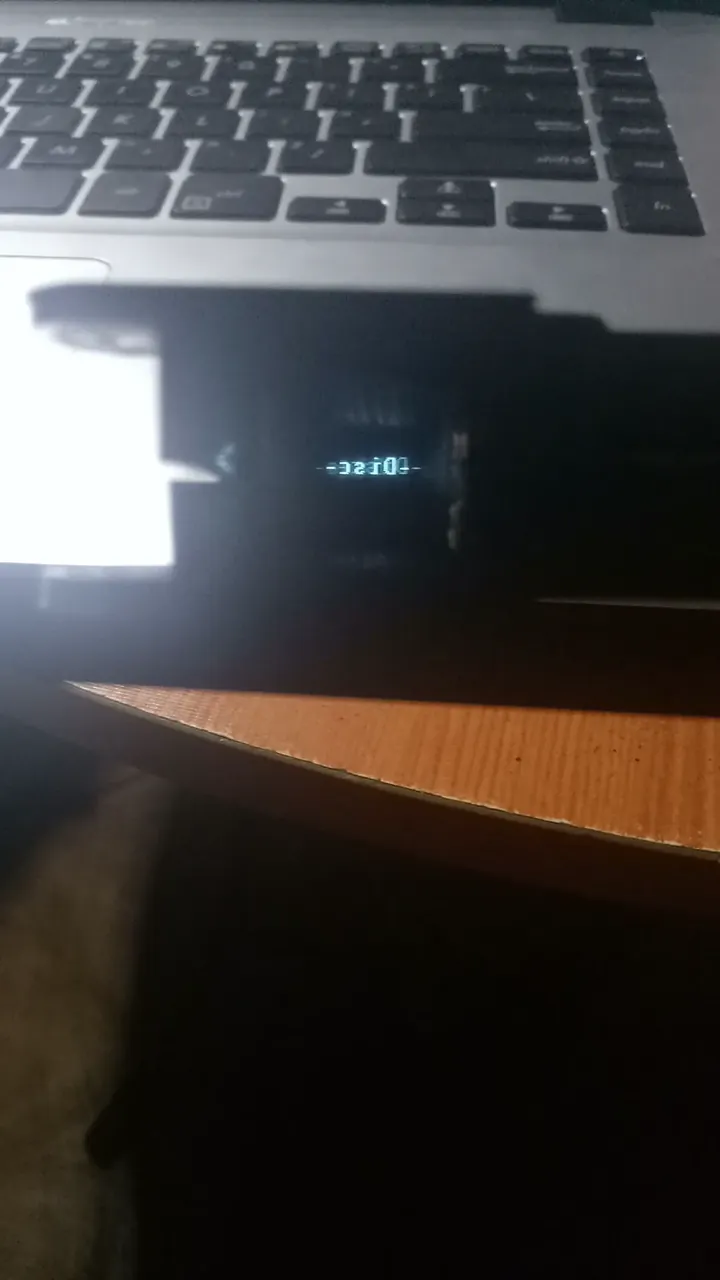 The device powered on, its OLED text floating in the reflector, seen from the front so it reads in mirror image