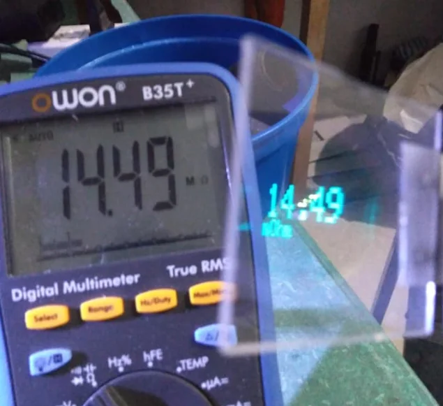 An OWON digital multimeter reading 14.49, with the same 14.49 floating in the Data Glass reflector beside it
