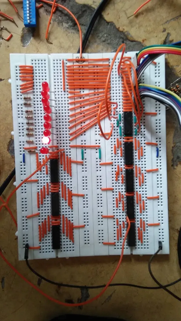 The tester on a breadboard: rows of orange jumper wires, a column of red LEDs with one lit, logic ICs down the middle, and a rainbow ribbon cable running off to the PC