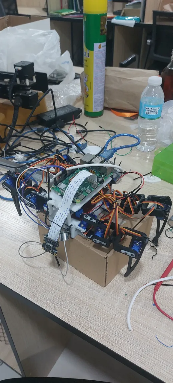 The quadruped prototype on a workbench: a Raspberry Pi and camera module on a white frame, ringed by servo legs and wiring